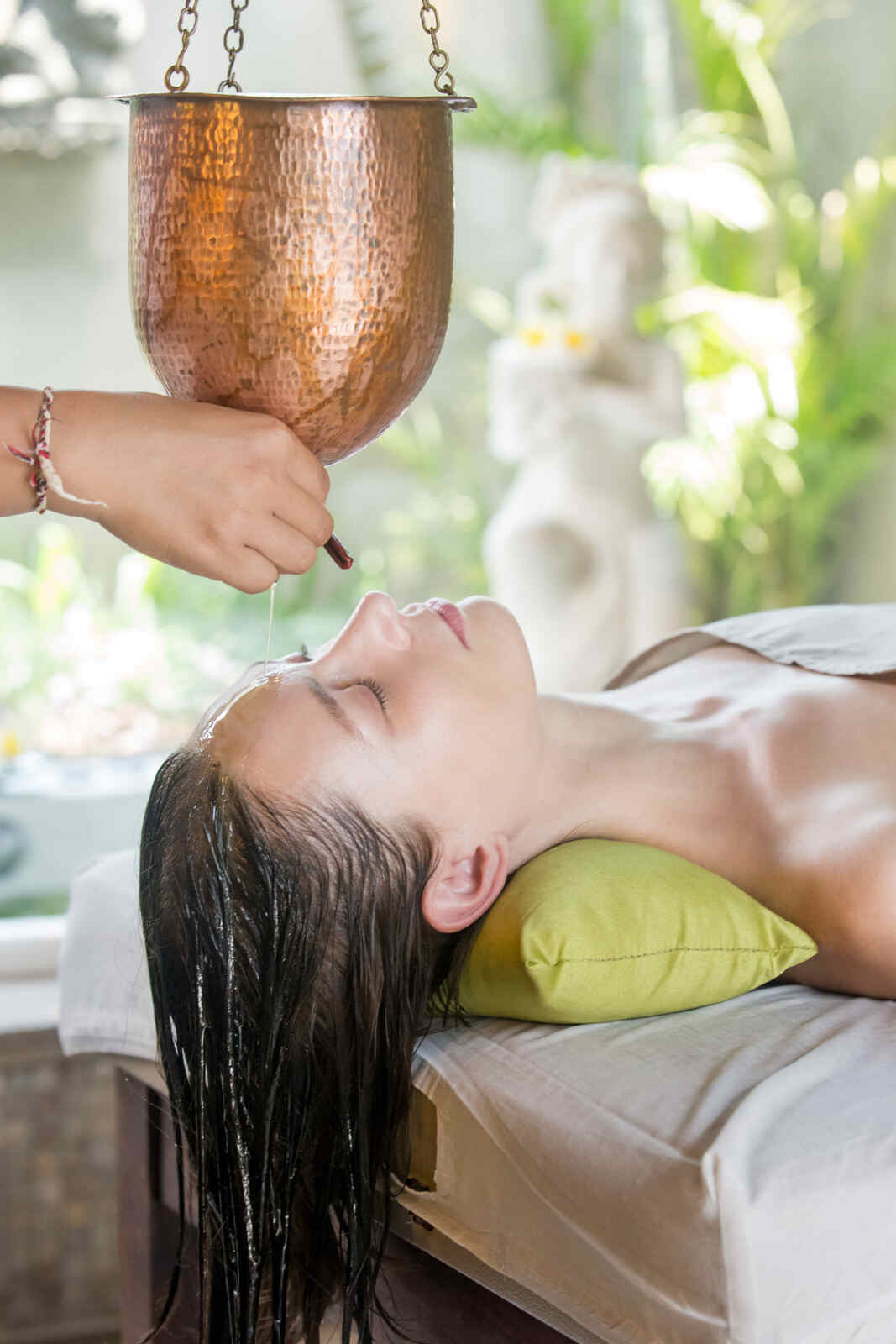 A woman receiving a traditional Ayurvedic oil therapy at Sai Ayush Ayurveda Hospital in KPHB, Hyderabad. The scene showcases a practitioner pouring oil from a copper vessel onto the woman's forehead, promoting relaxation and wellness in a serene setting.