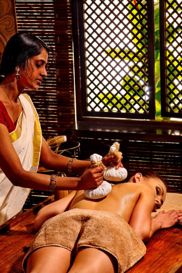 Ayurvedic therapist performing herbal massage for neck pain, utilizing poultices, on a client wrapped in a towel; part of Ayurvedic treatment in Hyderabad, 2025